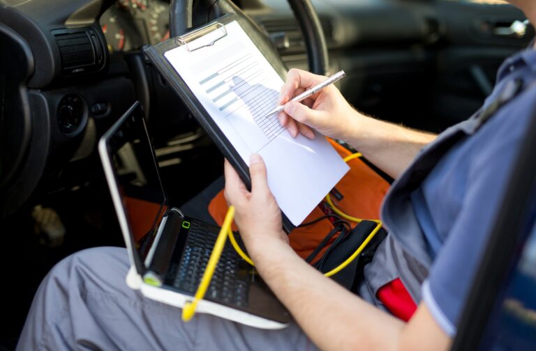 Fahrzeugdiagnose in der Werkstatt: Gutachter im Auto mit Laptop und Checkliste trägt Messwerte ins Inspektionsprotokoll ein.