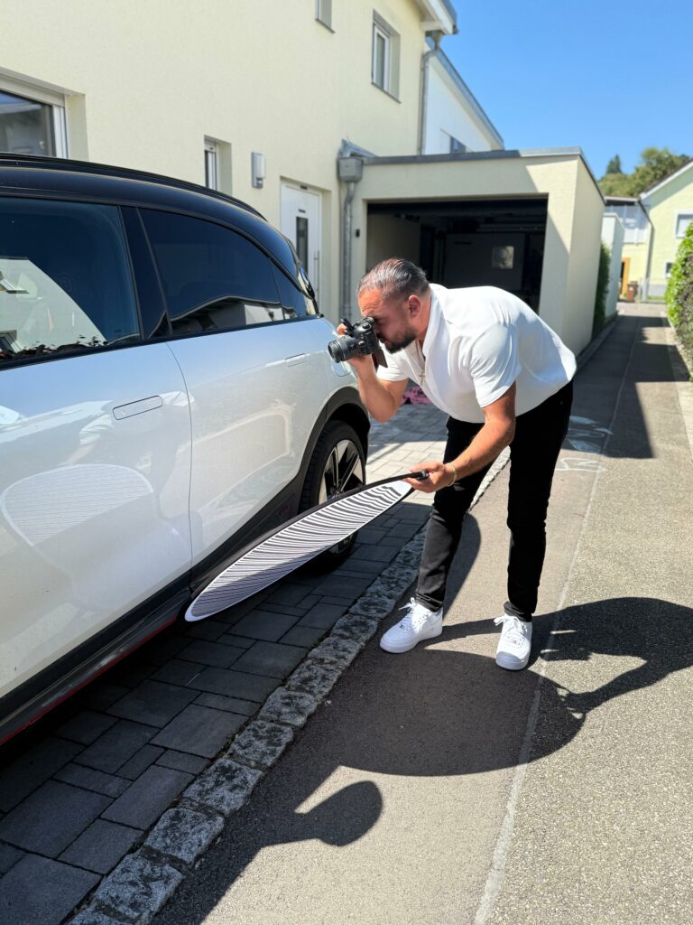 KFZ Gutachter dokumentiert Seitenschaden an weißem PKW mit Kamera und Reflektor – detaillierte Schadensaufnahme für Unfallgutachten.