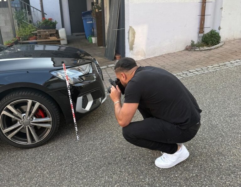 KFZ Gutachter fotografiert Frontschaden an schwarzem Auto mit Messstab – detaillierte Schadensdokumentation für Unfallgutachten und Wertgutachten.