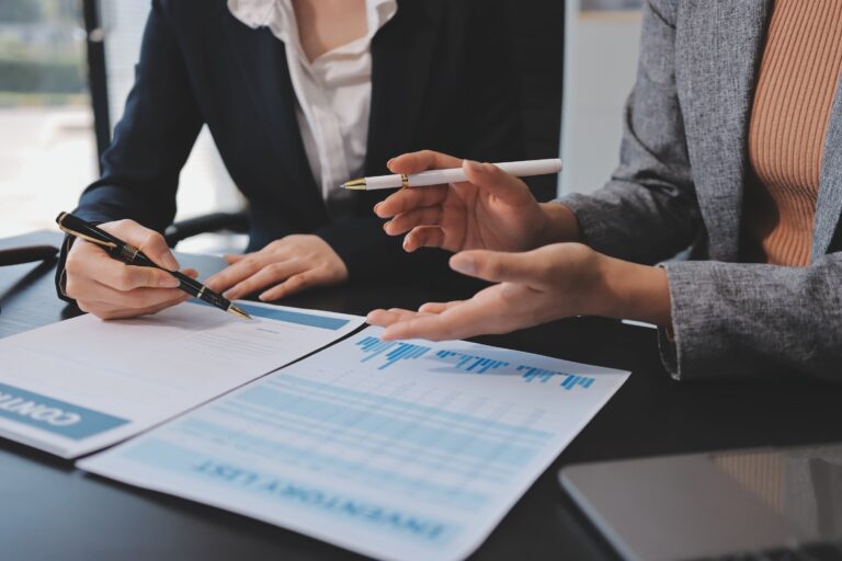 Beratungsgespräch: Hände in Businesskleidung zeigen mit Stiften auf Vertragsunterlagen und Diagramme.