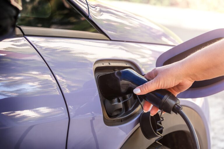 Hand steckt den Ladestecker in den Ladeanschluss eines Elektroautos (E-/Hybridfahrzeug).