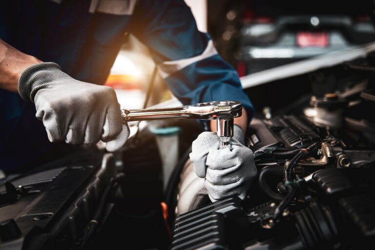 Mechaniker mit Arbeitshandschuhen zieht eine Schraube im Motorraum mit einem Schraubenschlüssel fest.