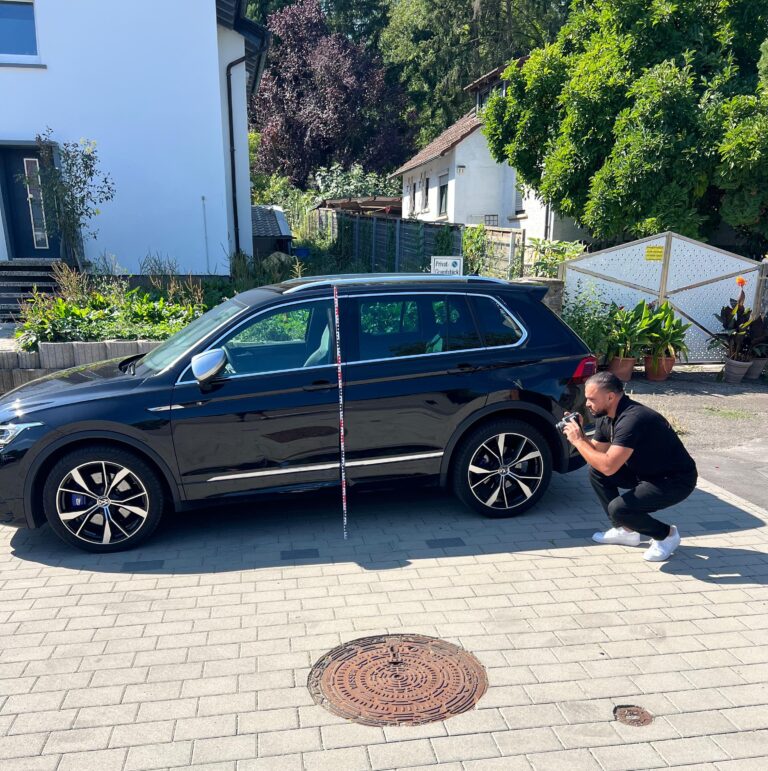 KFZ Gutachter fotografiert Seitenschaden an schwarzem SUV mit Messlatte – professionelle Beweissicherung für Unfallgutachten.