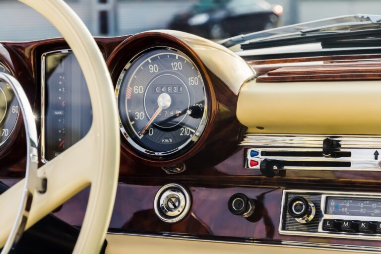 Detailaufnahme eines Oldtimer-Armaturenbretts (H-Kennzeichen) mit klassischem Tachometer, Holzverkleidung und cremefarbenem Lenkrad.